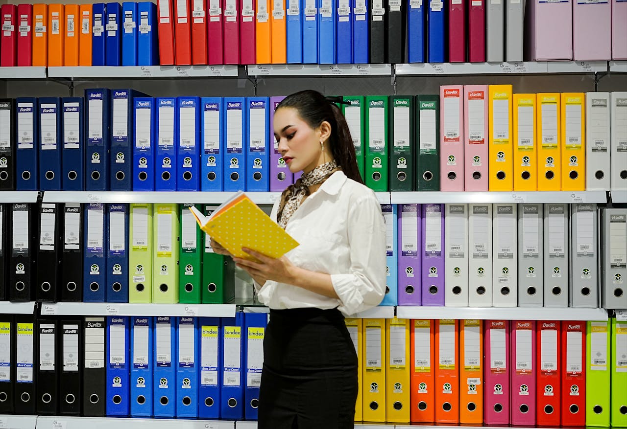 A young woman reads a file in front of a vibrant array of office binders.